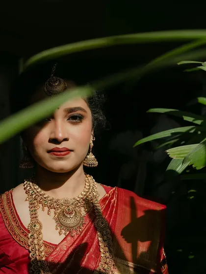 A creative portrait peeking through the leaves. Her makeup is striking yet natural, making her look like a goddess in a garden.
