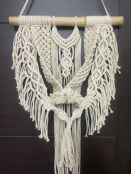 This handmade macrame wall decor features a unique central knot and cascading fringe. It's hung on a natural bamboo rod, adding to its rustic and organic feel.