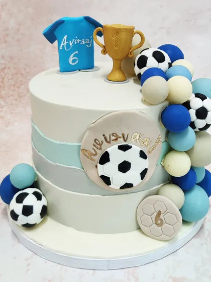 Our Football Champion Cake is perfect for a sports lover, featuring a jersey, trophy, and a cascade of footballs and spheres.