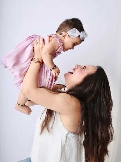 A classic mother-daughter pose, with the mother lifting her baby girl high in the air, both sharing a look of pure joy.