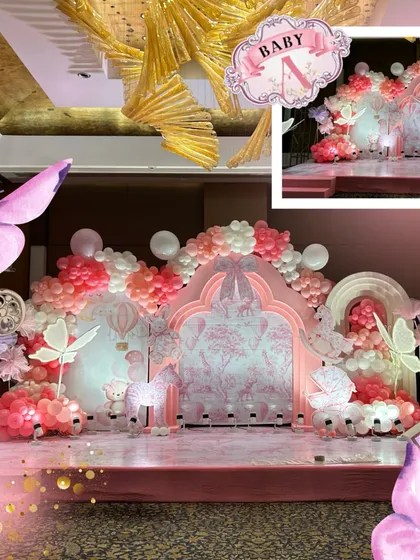 A detailed look at the pink stage backdrop, featuring a Dior-inspired print, butterfly accents, and a beautiful balloon arch in shades of pink, white, and coral.