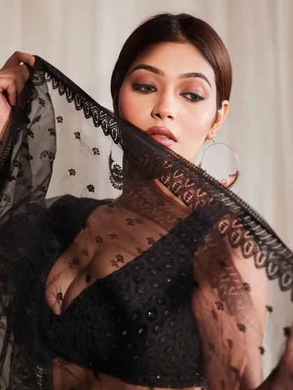A cinematic and moody portrait of a model in a black sheer lehenga, using the dupatta to create a mysterious and elegant veil effect.