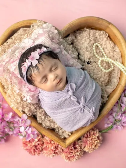 A fully swaddled newborn rests peacefully in a heart-shaped prop. The gentle wrap helps babies feel secure, allowing for these serene and beautiful poses.