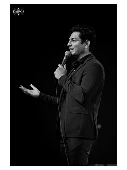 An actor or comedian mid-sentence, captured in a classic black and white style that emphasizes his expression and gesture.