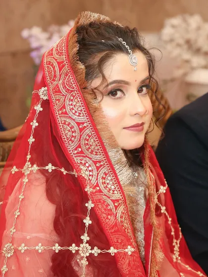 The bride under her red dupatta, a traditional touch to her modern engagement look.