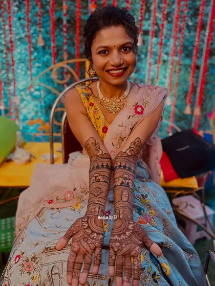 A happy bride showing off her gorgeous, traditional full-coverage mehendi. The design is packed with details, from the palms all the way up her arms.