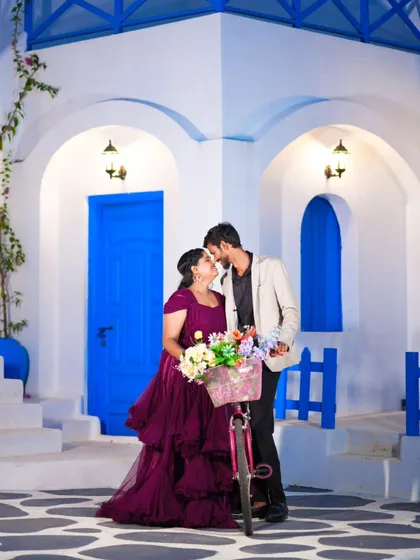 An intimate moment by a flower-adorned bicycle. The Santorini-style background makes this pre-wedding photo feel like a European getaway.
