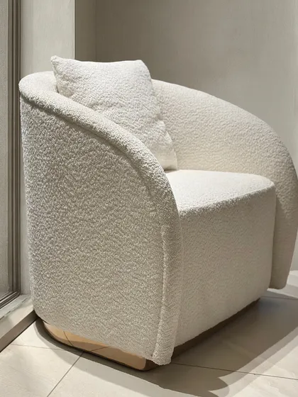 This angle shows the armchair's solid form and the subtle wooden base, grounding the soft, rounded design.