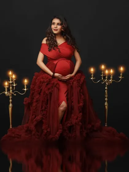 A vision in red. This mom-to-be is seated amidst candelabras in a voluminous red gown, her reflection captured on the floor for a stunning effect.