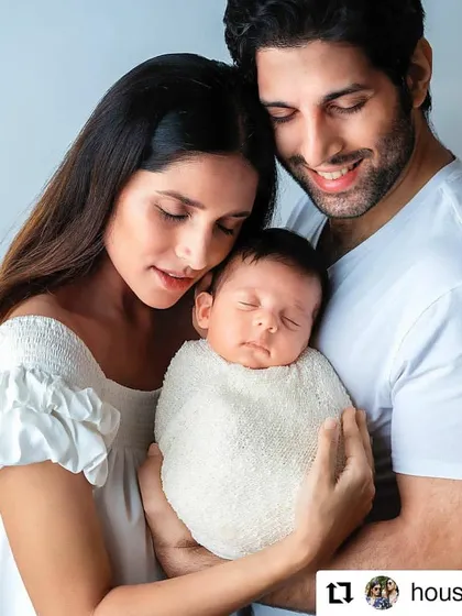 A beautiful family portrait, reposted from a happy client. The parents hold their swaddled newborn, their expressions full of love and joy.