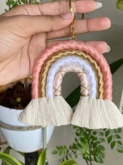 Holding up our pink and gold macrame rainbow keychain. The soft pastel colors make this a particularly popular choice for a gentle, boho-chic look.