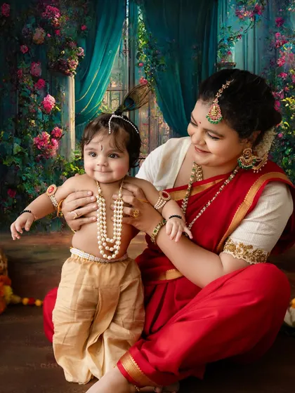 A candid and loving moment between mother and child. The baby, dressed as Krishna, smiles brightly, creating a heartwarming and authentic festival portrait.