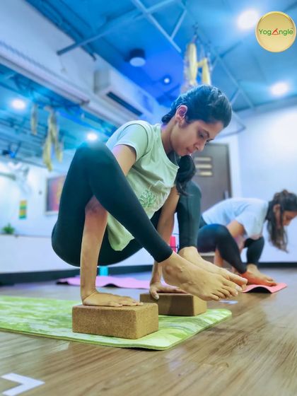 Building arm strength for poses like Bhujapidasana takes time. Here, a student uses blocks to elevate her hands, making the arm balance more accessible while she develops the core and upper body strength required.