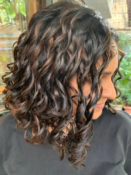 A side view of this curly brown bob. The non-bleach highlights add beautiful dimension to the short cut.