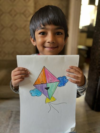 A young boy smiles with his colourful kite drawing for Makar Sankranti. We celebrate this festival by creating art that is full of movement and joy.