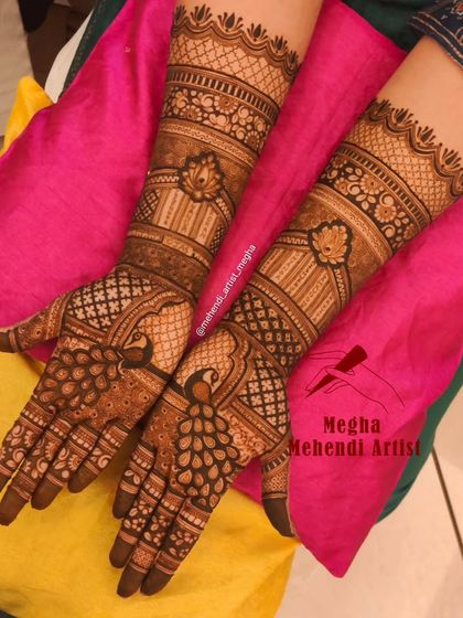 Full-arm mehendi featuring graceful peacocks on the palms and jharokha-inspired patterns on the forearms for a truly grand statement.