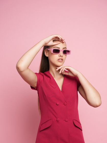 A close-up shot of a model in a pink blazer dress, styled with pink rectangular sunglasses. This highlights the playful yet chic vibe of the collection.