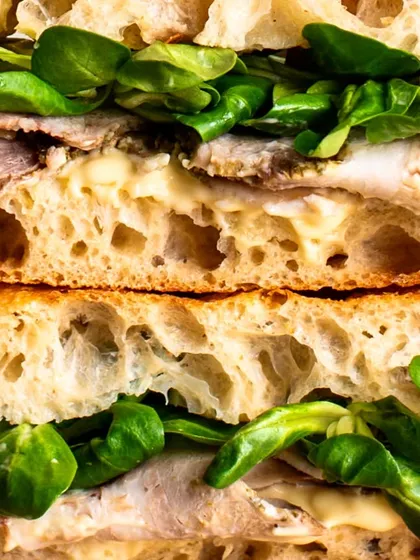 A detailed close-up of a roast beef sandwich, showcasing the layers of tender meat, fresh greens, and creamy sauce.