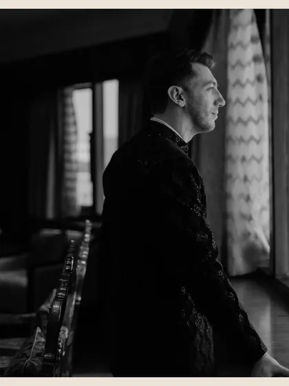 A moody, vintage-toned profile shot of the groom looking out a window, lost in thought before the ceremony.