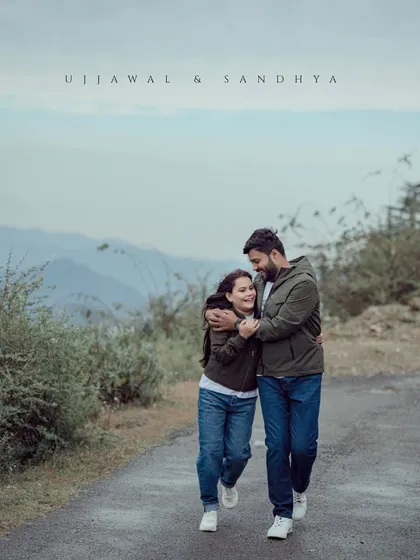 A couple walks together on a quiet mountain road, their matching jackets and shared embrace creating a sense of unity and companionship.