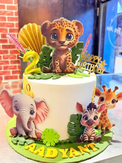 A cute jungle-themed cake for a 2nd birthday, featuring a baby leopard, elephant, zebra, and giraffe.