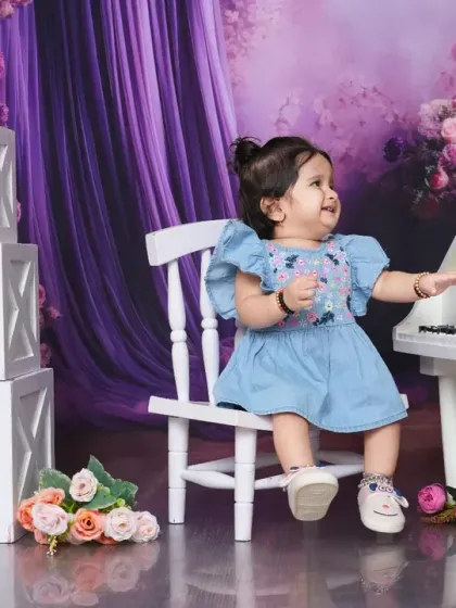 A baby girl reaches for the keys of a miniature piano, surrounded by flowers. This shot captures a moment of curiosity and discovery in a beautiful setting.
