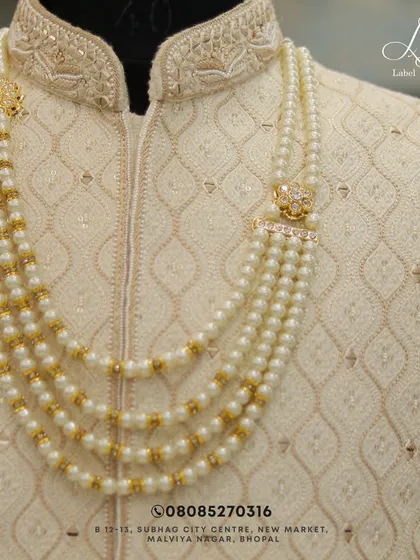 Another look at the fine details. The layered pearl necklace with gold accents sits perfectly on the textured fabric of this custom sherwani.