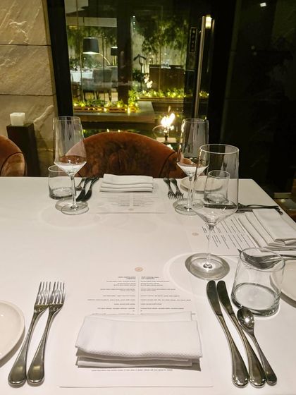 A table set for dinner, with the warm glow of the restaurant and the garden lights reflected in the window. It’s a space designed for nights you’ll remember.