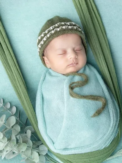 A baby boy sleeping in a green sling, looking so peaceful in his little knitted hat.