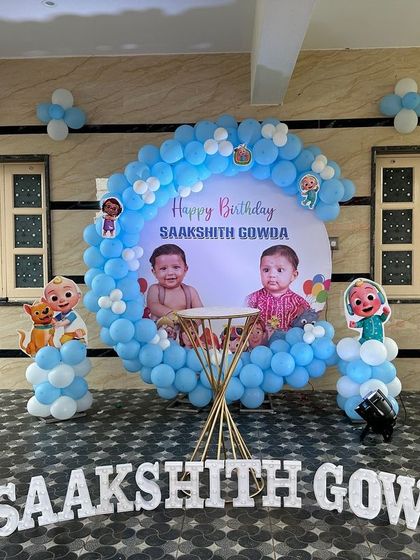 A simple and sweet Cocomelon theme for twins. The circular backdrop is personalized with their photos, framed by a blue and white balloon arrangement.