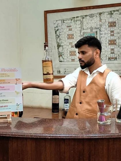 A bartender performs a bottle balancing trick behind the bar next to a custom-printed drink menu. This showcases how we integrate our flair skills directly into the bar service experience.