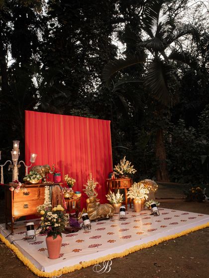 The full view of the reception stage featuring an upcycled red dupatta as a vibrant backdrop. The setup includes a floor covering, antique furniture, and floral arrangements, creating a complete and personalized photo corner.