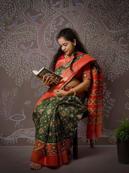 A quiet moment during a traditional maternity shoot. The expecting mother reading a book against the Worli art backdrop adds a layer of storytelling and personality.