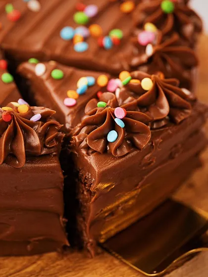 A close-up shot of a rich chocolate cake, focusing on the glossy frosting and colorful sprinkles. Taking out one slice creates a dynamic composition and makes you feel like you're about to take the first bite.