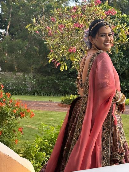 The bride looks stunning in her wedding lehenga, with her hair styled in a beautiful bun adorned with pastel-colored flowers. The look is perfect for a daytime wedding.
