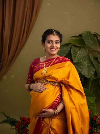 A classic portrait of a mother-to-be in a stunning yellow and red silk saree. Her happy expression and the traditional jewelry complete this elegant and joyful look.