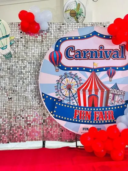 A fun photo booth area for a carnival party, featuring a shimmering silver wall and a large circular carnival-themed backdrop.
