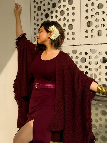 A serene moment in my burgundy poncho look. The flower in my hair adds a soft, organic touch to the dramatic outfit.