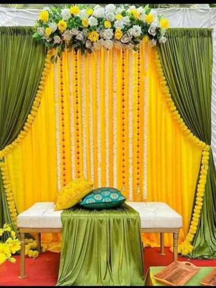 Elegance can be simple. This backdrop uses a beautiful combination of olive green and bright yellow drapes, accented with marigold garlands and a floral header. The two benches provide comfortable and stylish seating for the couple.