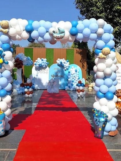 A grand entrance arch for a baby boy's welcome party. The blue and white balloon arch is decorated with small teddy bears and leads to a red carpet entrance.