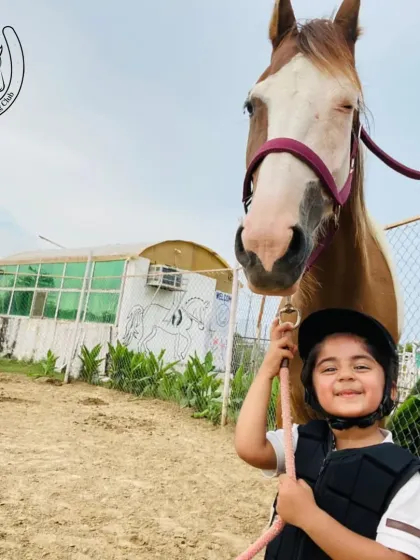A young boy proudly holds the reins, standing next to his new four-legged friend in our sandy arena.