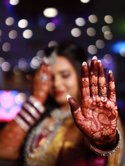 A beautiful, artistic shot focusing on the bride's hand against her colorful reception outfit. The shallow depth of field makes the rich mehendi stain pop.