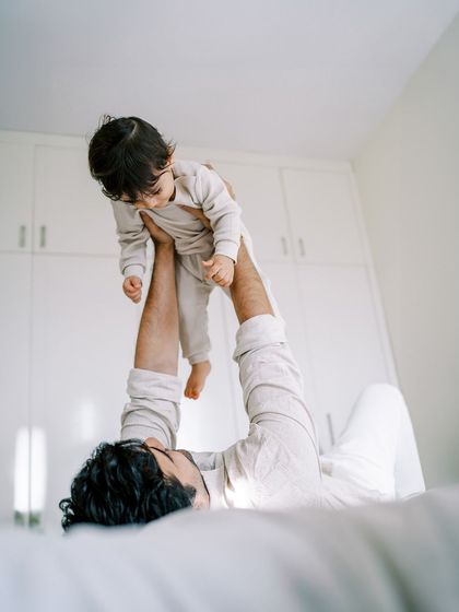 A father lifting his son in the air while lying on the bed. A fun and playful perspective.