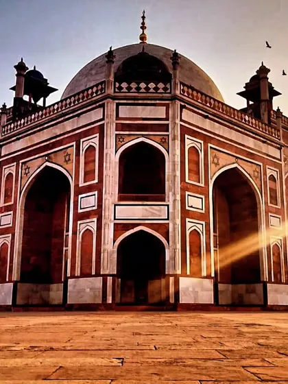 A dramatic shot of Humayun's Tomb with sun rays breaking through. The building's perfect symmetry and garden setting were designed to represent a paradise on Earth.