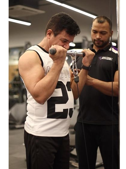 A trainer provides spotting and encouragement to a member during a set of cable bicep curls, helping him push past his limits.