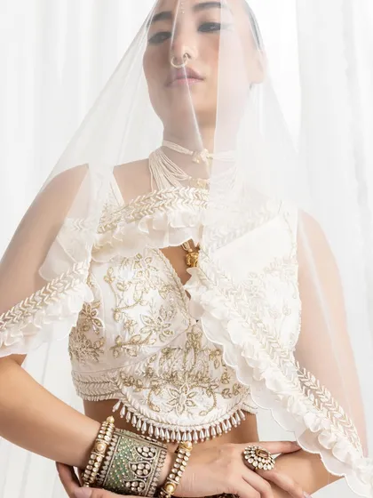 An ethereal shot with a focus on bridal jewelry. The model is seen through a sheer veil, with the intricate polki bangles and statement ring becoming the central elements of this soft and romantic image.