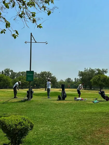 A group of golfers practicing on the grass tees on a clear, sunny day.