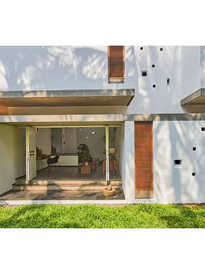 A ground-level view of the Aayi House, showing how the living room opens directly onto the lawn. The design erases the boundary between the indoor and outdoor living areas.