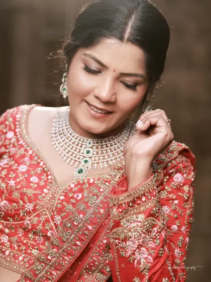 A soft and intimate close-up. The focus is on the bride's gentle smile and the exquisite diamond and emerald necklace, showcasing luxury and elegance.