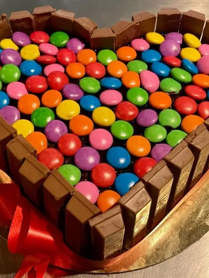 A fun and indulgent heart-shaped cake for the ultimate chocolate lover. This cake is bordered with KitKat bars and filled to the brim with colorful Gems, combining two favorite treats in one.